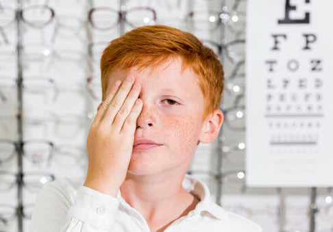 cute-boy-covered-his-eye-with-hand-standing-optics-clinic-1